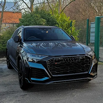 A black car parked in front of a green fence.